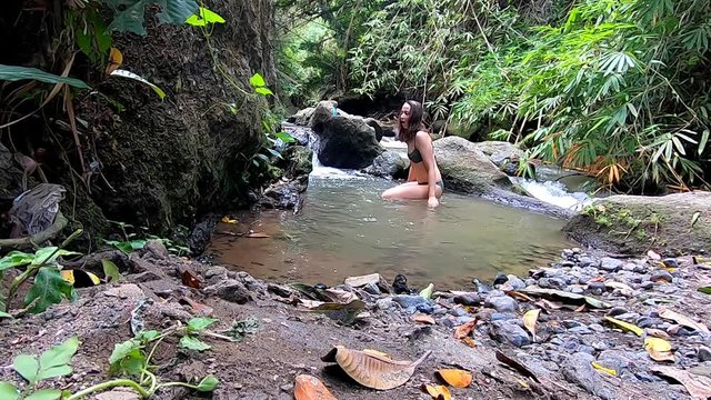 Slim, caucasian woman in a green bikini travelling as a backpacker in Ubud, Bali, bathing and relaxing in a tropical river in the rainforest as she is practising a nature connected lifestyle