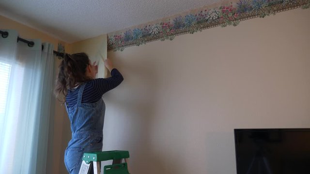 Young woman peels off outdated floral wallpaper border