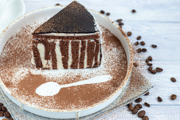 A slice of zebra cake with chocolate icing. On a light background. In the background is a cup of coffee. Coffee beans are scattered throughout.