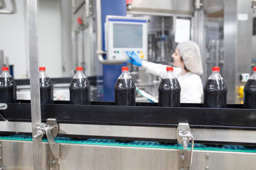 Young happy female worker in bottling factory checking juice bottles before shipment. Inspection quality control.