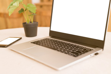 Fototapeta premium A workplace in a bright kitchen during quarantine. Laptop with place for text. Telework. freelance. flowerpot, phone and cup on the table.Copy space.