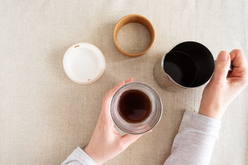Female hand holding reusable glass cup with black coffee on natural linen background. Reuse, reduce, recycle and no plastic concept.