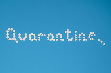 Fototapeta premium The word quarantine, laid out with white tablets on a blue background horizontally. Coronavirus, quarantine concept. Selective focus. Horizontal orientation. View from above.