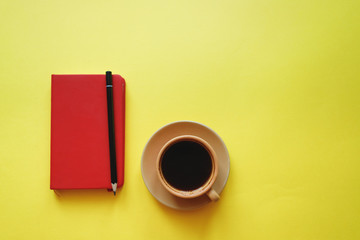 cup of coffee on yellow background with notepad