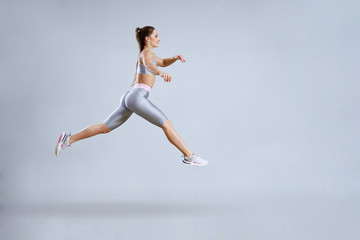 Fit woman doing cardio training in gym. Woman in sportswear is jumping. Fitness club concept. Isolated on a gray.