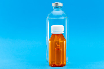 glass bottle with injection and orange plastic bottle with a yellow cap and an ampoule with a vaccine inside, medical concept on a blue background with copy space.