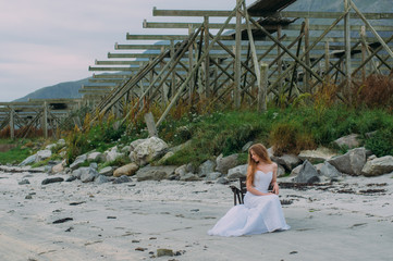 Fototapeta na wymiar Bride sitting on chair on beach with white sand, fish dryers on background