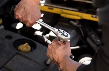 Car mechanic doing engine repair using socket wrench key. 