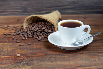 White cup of coffee. On a wooden background. Coffee beans are scattered all over the surface.