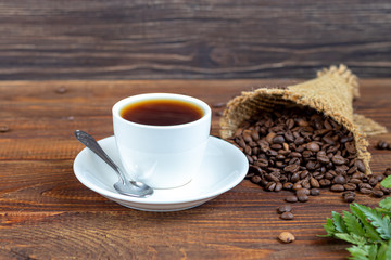White cup of coffee. On a wooden background. Coffee beans are scattered all over the surface.