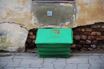 Green plastic sand box standing on pavement beside old crumbly wall