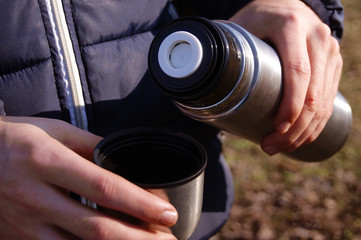Man's hands pouring fresh hot cocoa from thermos to cup.