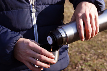 Man's hands pouring fresh hot cocoa from thermos to cup.
