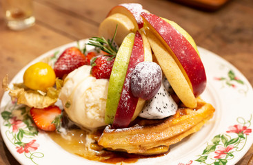 Whole waffle topped with syrup, whipped cream, ice cream and seasonal fruits. Delicious sweet waffles with fruits on rustic wooden table. Waffles with fresh fruits on rustic wooden background.