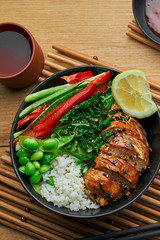 Couple of delicious Buddha bowls with teriyaki chicken, fresh vegetables, edamame soy beans and basmati rice with green tea on a wooden table. Top view, directly above shot.