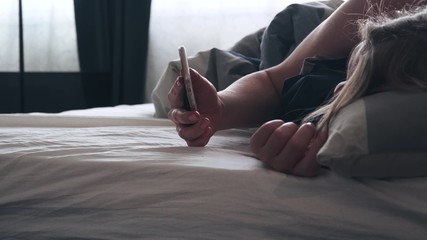Fototapeta premium girl in bed check her phone for alarm clock and looks at screen than put away.
