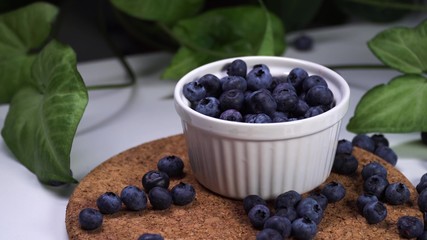 delicious blueberries falling in white bowl. cinematic view with green plants in the background