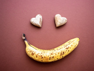 Überreife Banane mit Punkten und zwei Herzen in Gesichtsform, brauner Hintergrund, Draufsicht, Humor