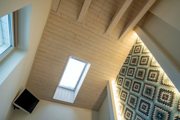 Wooden ceiling in a contemporary mansard room with attic window ob decorative planks surface.
