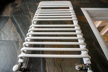 White contemporary electric towel dryer mounted on black tiled wall in modern bathroom.