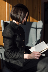 Obraz premium Portrait of young adult woman sitting in a chair and reading books, slow living or leisure concept. selective focus