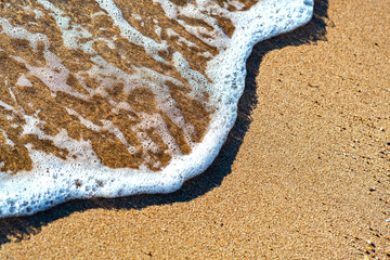 Fototapeta na wymiar Close up of small sea waves with clear blue water over yellow sand beach at summer sunny shore.