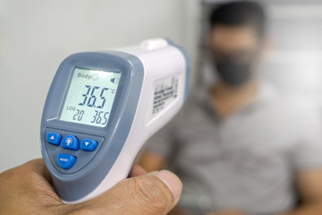 Hand holding infrared thermometer to measuring temperature on blurred asia people with face mask on background. Covid flu screening 19 concept. - obrazy, fototapety, plakaty