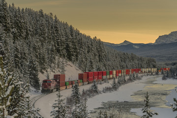 Freight train with containers after picturesque Morant's curve on a cold winter evening with sun just setting behind majestic mountains. © Anze