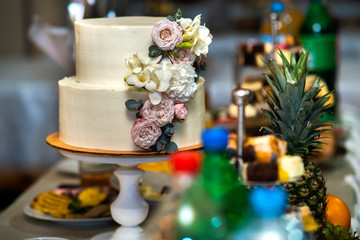 Tall sweet wedding cake decorated with live pink and white flowers on a table.