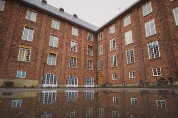 Large industrial red brick house, with visible reflection on the ground in a pool of water. Autumn cold setting, good for background