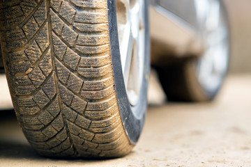 Close up of dirty car wheel with rubber tire covered with yellow mud.