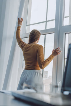 Smart Working, Agile, Remotely Working, Flexible Hours, Rearranged Offices, New Way Of Organising Work. Employees  Work From Home. Young Woman Stands At Window In Her Home On Laptop Background