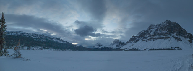 Wide mountain panorama during early winter morning on Bow Lake, Canada. View of the frozen lake at the sunrise.