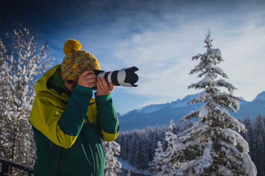 A Man is photographing beautiful snowy mountain scenery. Man in winter clothes and telephoto lens taking pictures of a beautiful mountain landscape. Picture from side.
