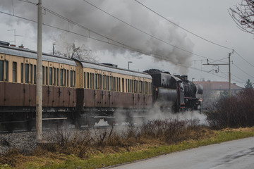 Old vintage steam train with black locomotive is running full power on a railroad track in the city...