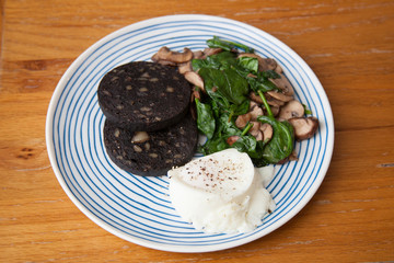 A breakfast of black pudding, spinach, poached eggs and mushrooms