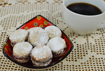 Traditional serbian vanilla cookies with jam, vanilice, in the red bowl, with cup of coffe in the background