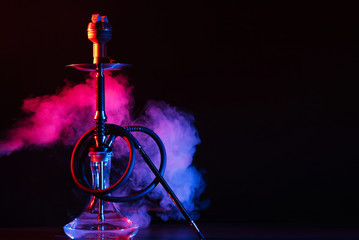 glass hookah shisha with a metal bowl on the table on a black background with smoke - obrazy, fototapety, plakaty