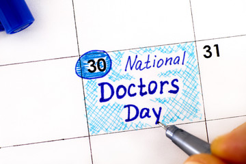 Woman fingers with pen writing reminder National Doctors Day in calendar.