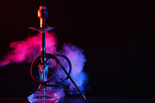 glass hookah shisha with a metal bowl on the table on a black background with smoke