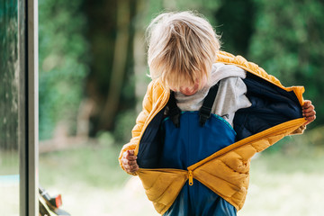 Kleinkind in Regenhose zieht seine Jacke aus