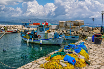 Fototapeta na wymiar Beautiful landscape with old small fisher boat, colorful fishing nets, calm sea water, blue sky with clouds and mountains on the horizon. Corfu Island, Greece.