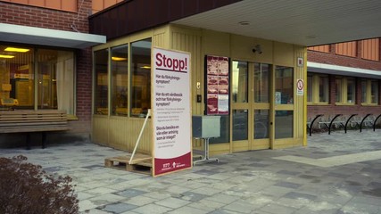 A partly closed hospital in Sweden with a big STOP sign telling you not to enter if you suspect that you are, or might be infected. Camera panning from right to left. Filmed in slow motion at 4K. - Powered by Adobe