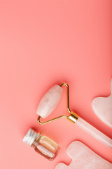 A set of tools for face Massage technique Gua Sha made of natural rose quartz on a pink background. Roller, jade stone and oil in a glass jar for face and body care.