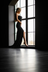 Fototapeta na wymiar Gorgeous blonde in a black tight-fitting dress in contrast to the window with the frame
