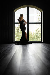 Gorgeous blonde in a black tight-fitting dress in contrast to the window with the frame