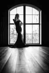 Fototapeta na wymiar Gorgeous blonde in a black tight-fitting dress in contrast to the window with the frame. Black and white