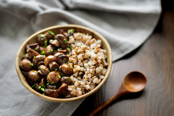 Sauteed white mushrooms with buckwheat in wooden bowl