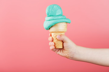Ice cream in a child's hand melts on a pink background. The waffle cone with blue ice cream melts.