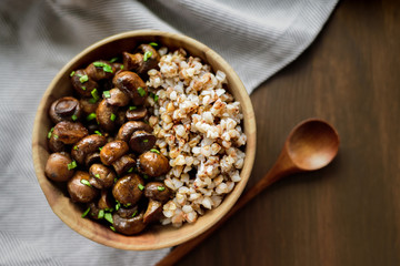 Sauteed white mushrooms with buckwheat in wooden bowl